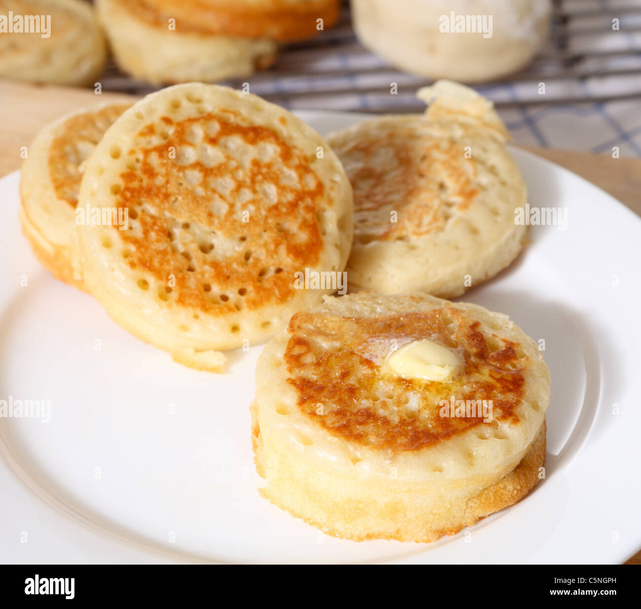Traditional English homemade crumpets with a knob of butter on the front one. Stock Photo