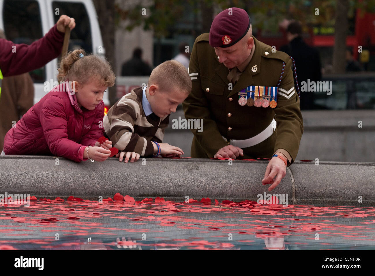 A soldier throws poppys into the Trafalgar Square fountain with his children on Remembrance day. Stock Photo