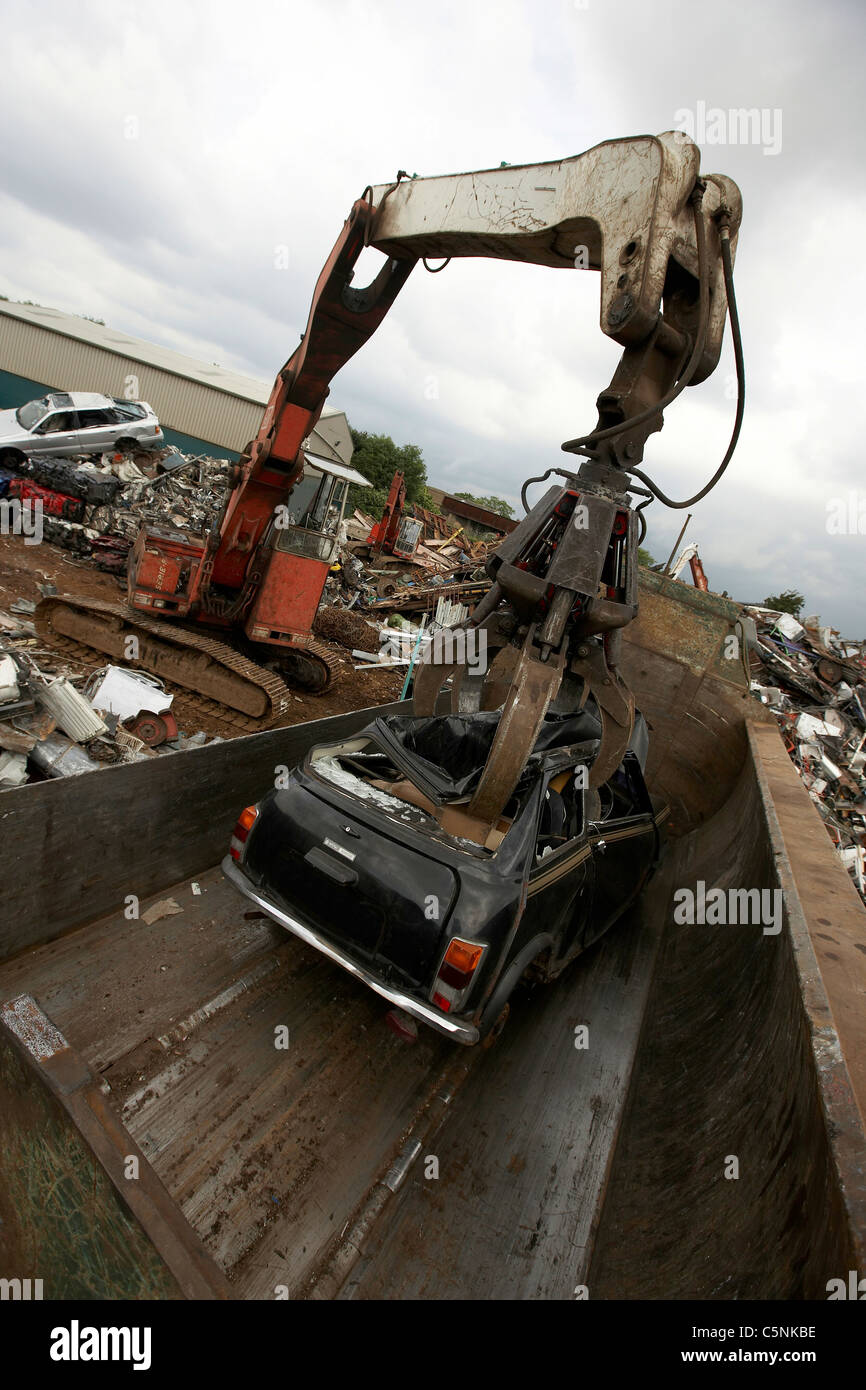 Crane lifting scrap car into a car crusher for recycling in a scrapyard