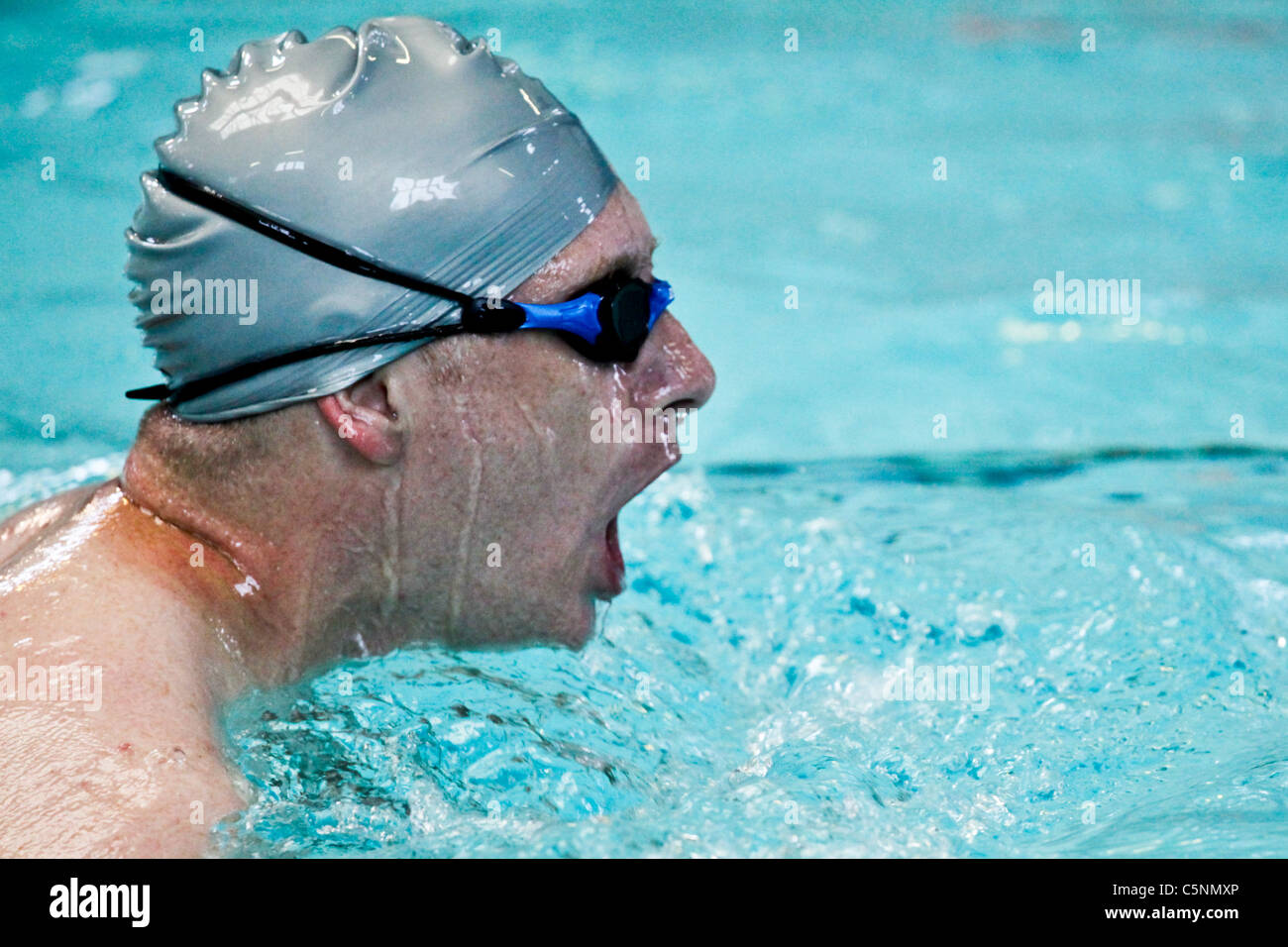 Indoor swimmer in a silver swimming cap and goggles swimming freestyle