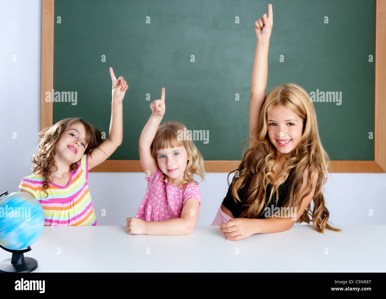 kids student clever girls group in classroom raising hand finger with blackboard Stock Photo