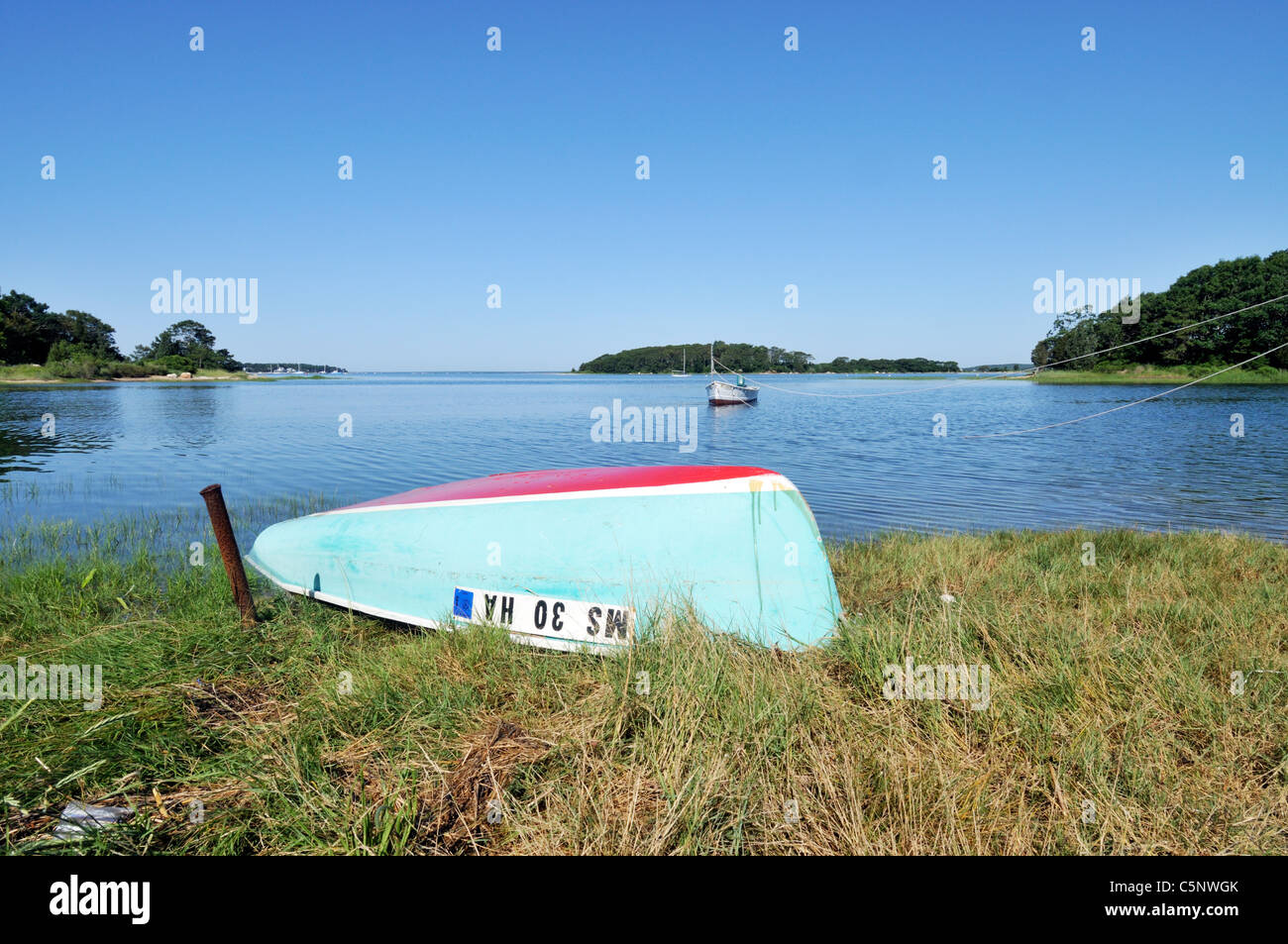 Small boat overturned on seagrass at waters edge of a Cape Cod harbor. USA Stock Photo