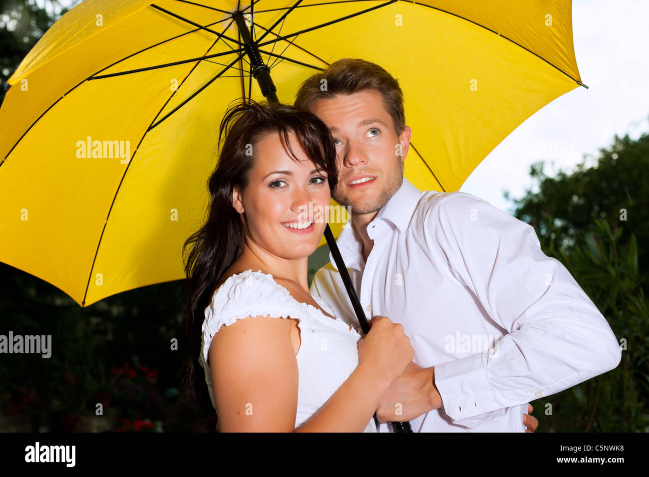 Happy couple in the summer rain with a yellow umbrella Stock Photo