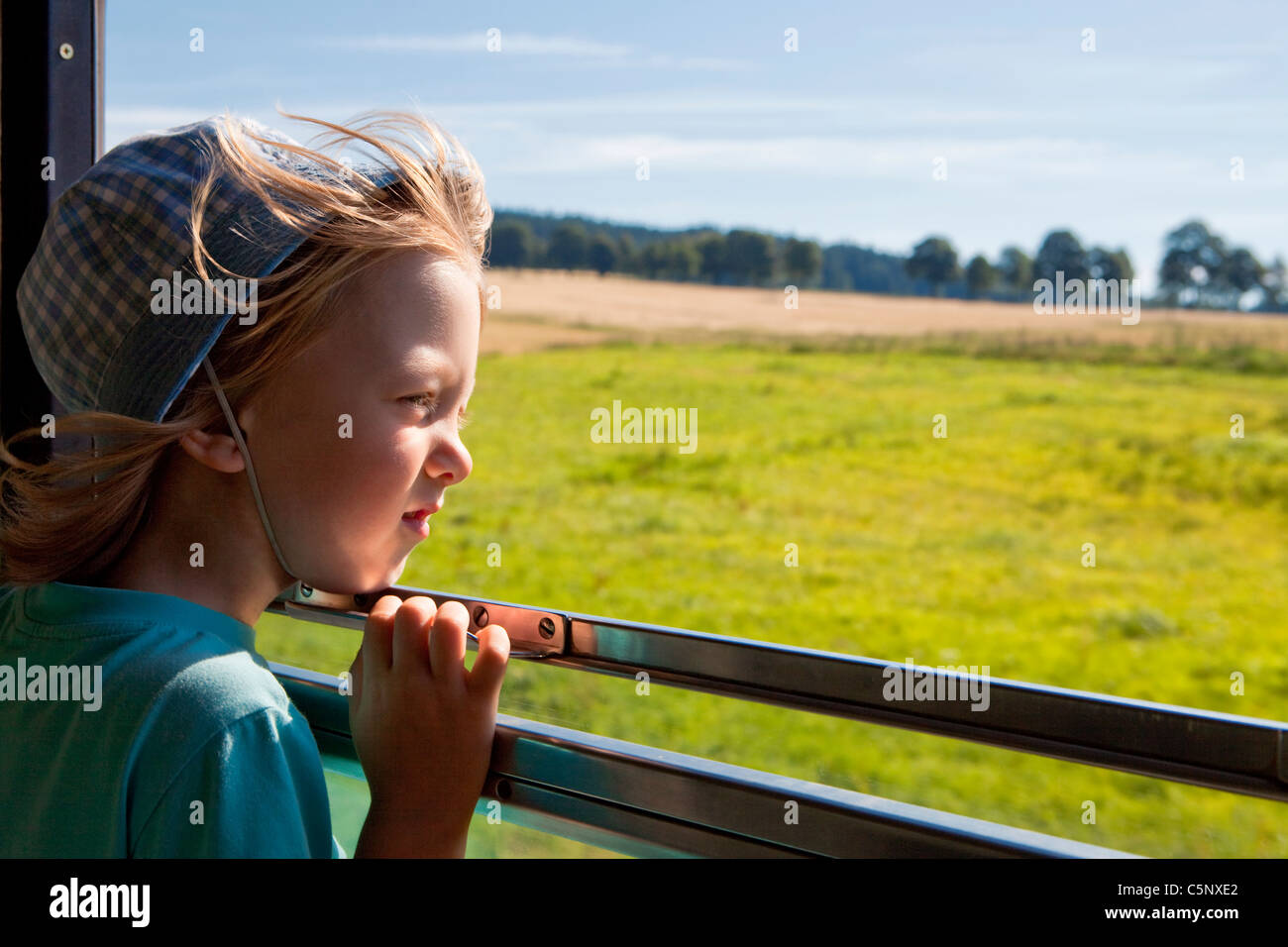 boy with long blond hair and hat looking out the train window Stock Photo