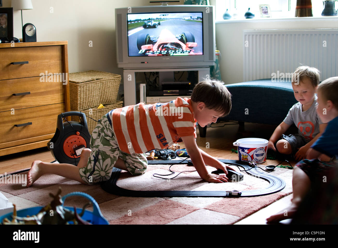 Boys playing Scalextric electric car racing game whilst grand prix is shown on TV,Sky Sports has won the rights to show f1 Stock Photo