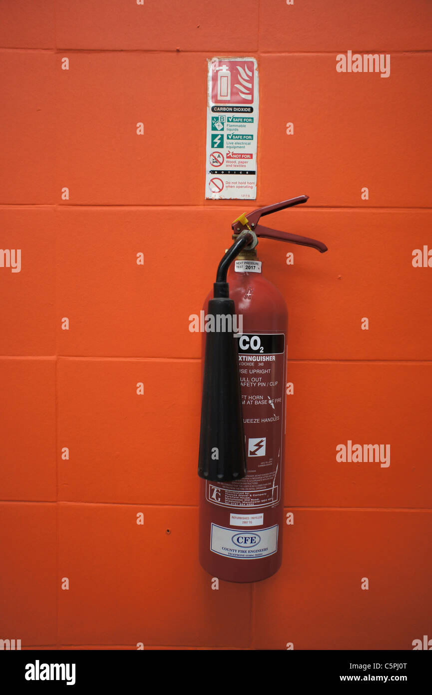 Fire extinguisher mounted on an orange coloured block wall, with
