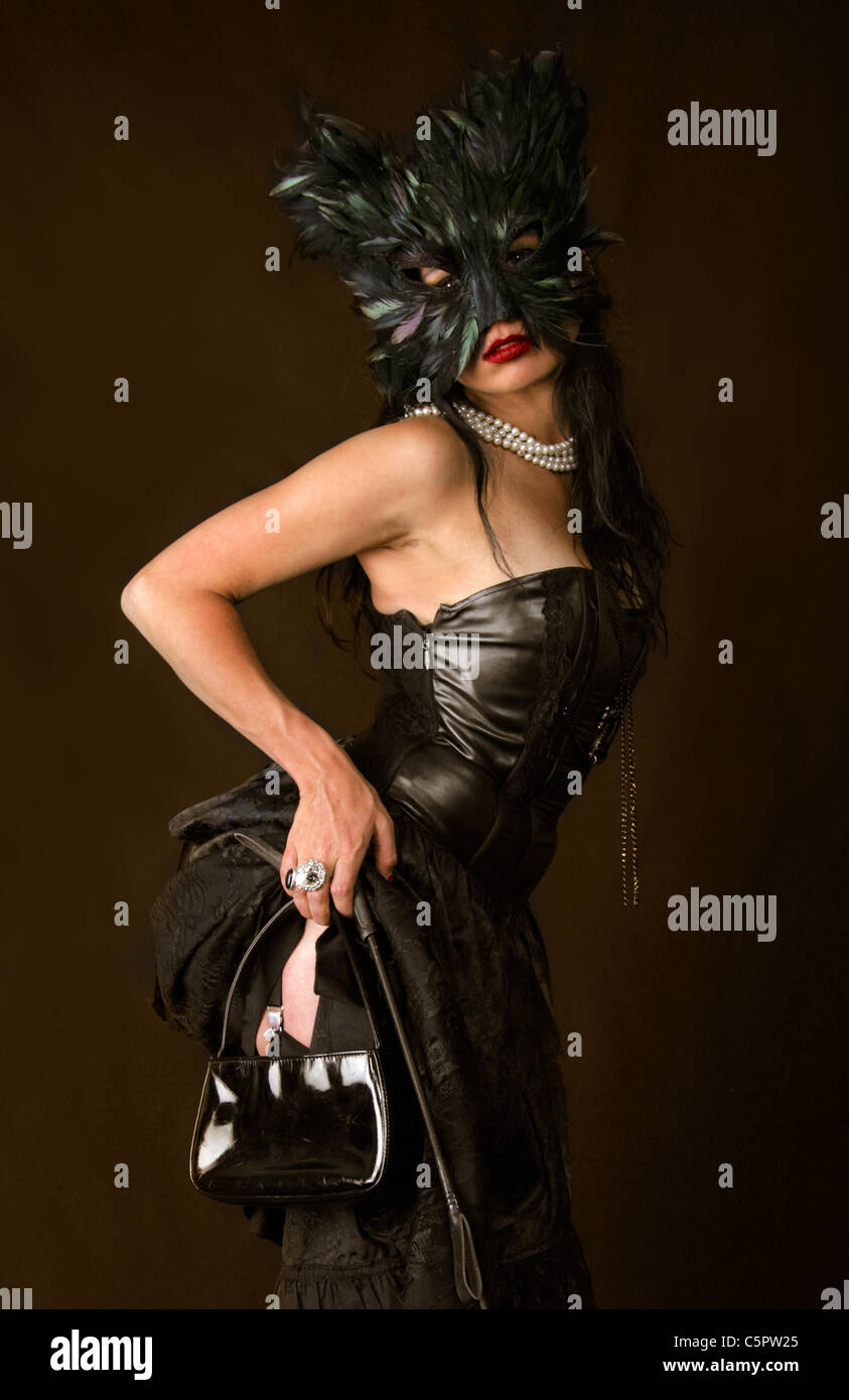 Girl in a Black Dress Wearing a Black Cat Mask with Riding Crop and Handbag. Stock Photo
