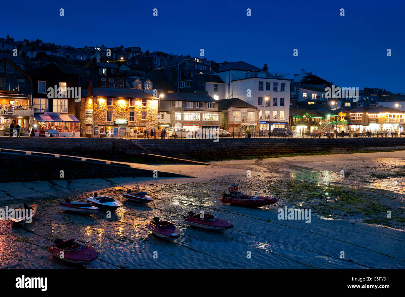 St Ives harbour at night featuring well lit bars and restaurants along with a low tide. Stock Photo
