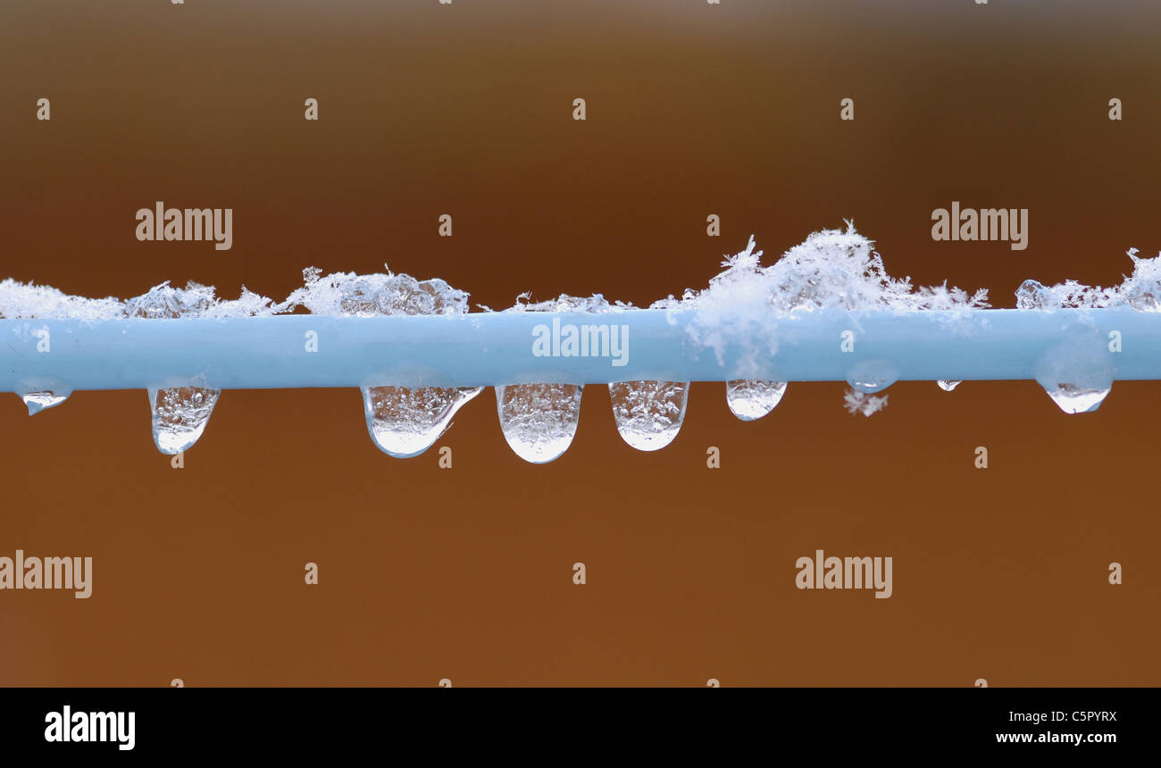 Snow crystals melting on washing line with water droplets forming below. Stock Photo