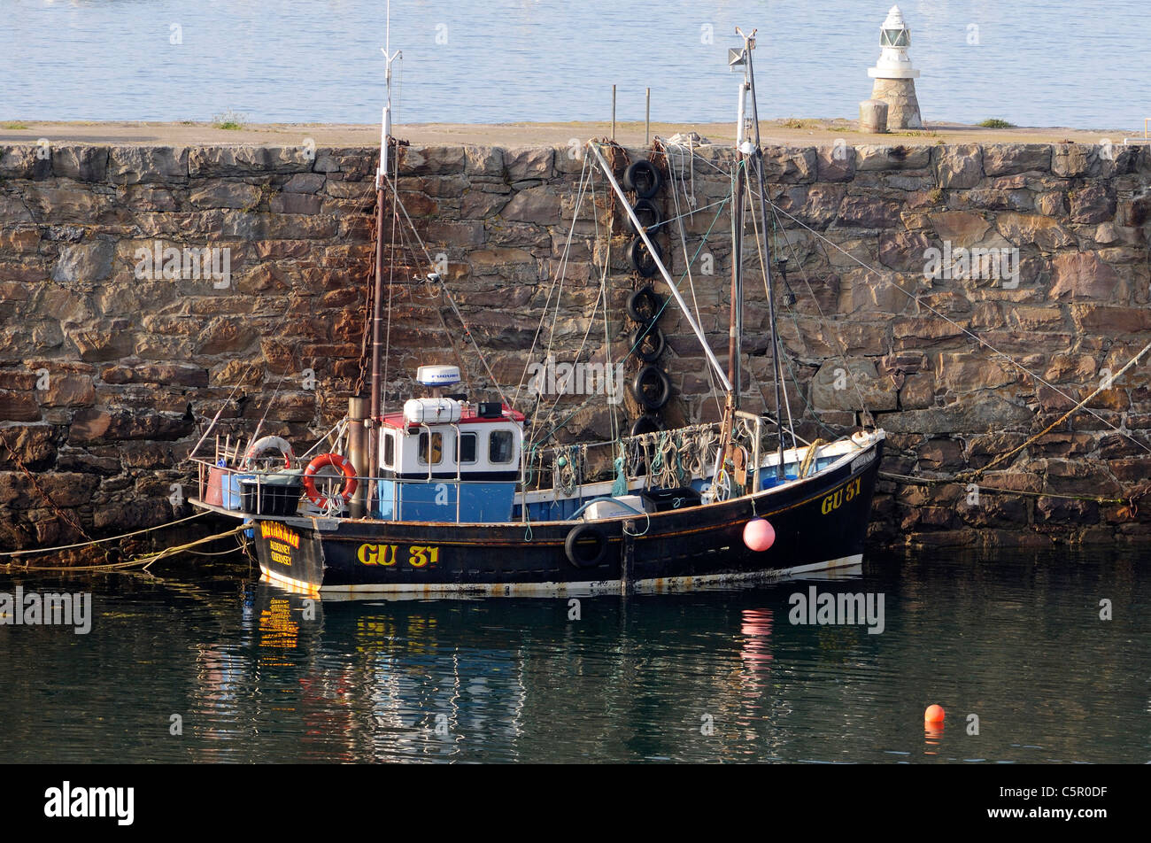 A fishing boat tied up against the  Braye Harbour breakwater.  Alderney, Channel Islands, UK. Stock Photo