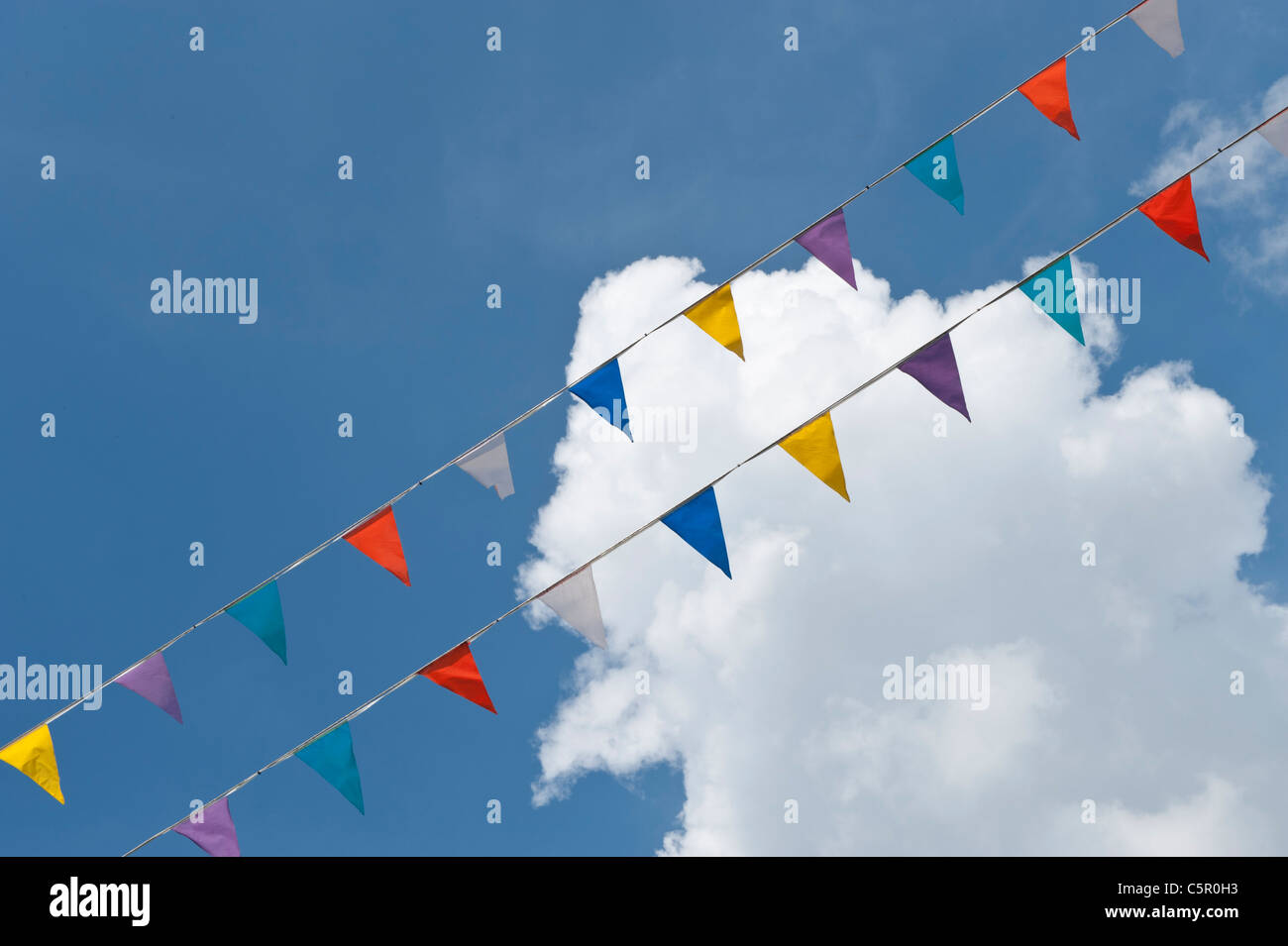 Strips of colourful bunting line diagonally across a sky slightly covered by patchy cloud in Christchurch, Dorset. Stock Photo