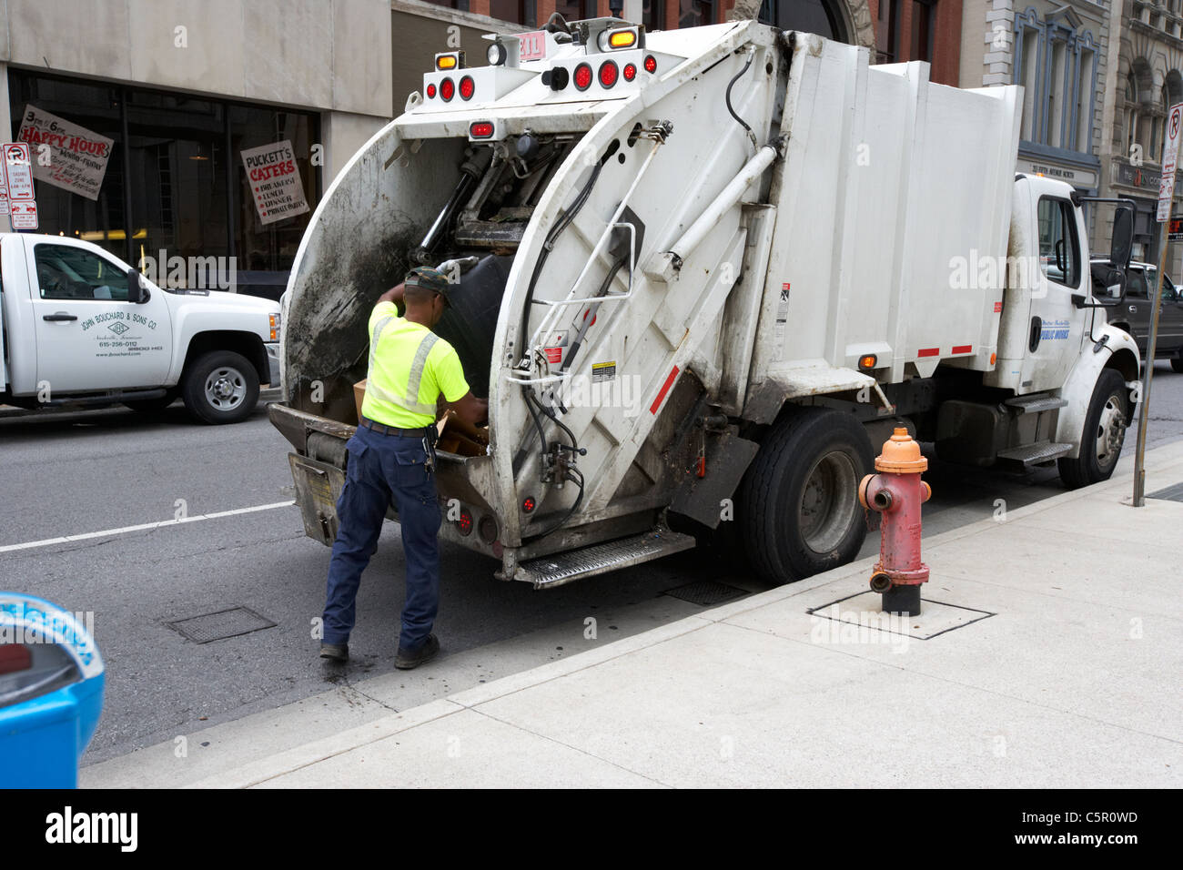 african american city worker emptying garbage into refuse truck