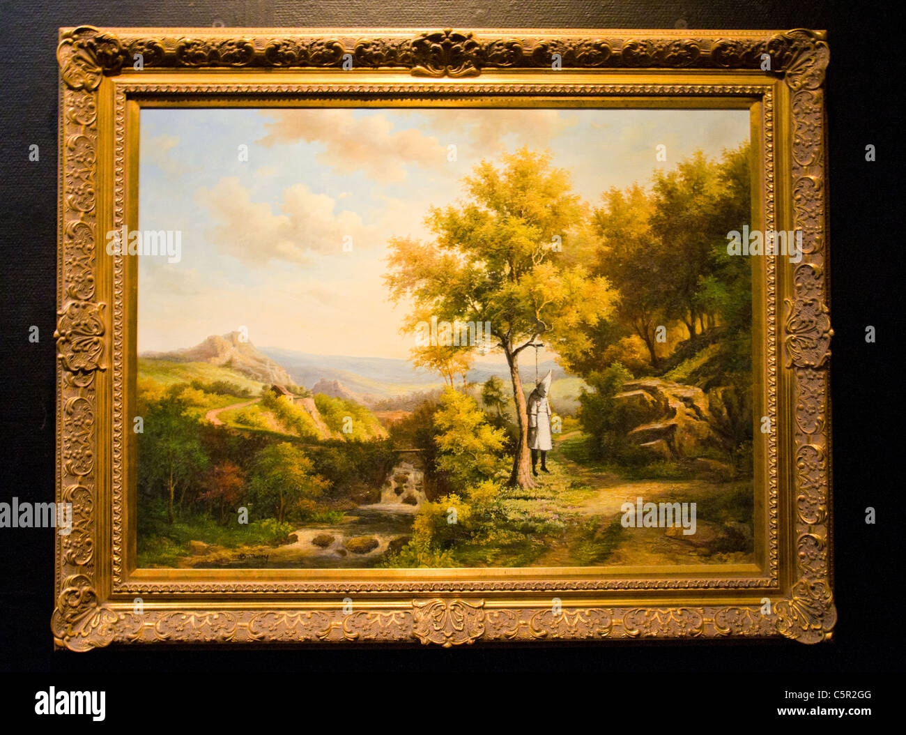 Banksy picture of lunched Ku Klux Klan member hanging from tree in classic rural painting Stock Photo
