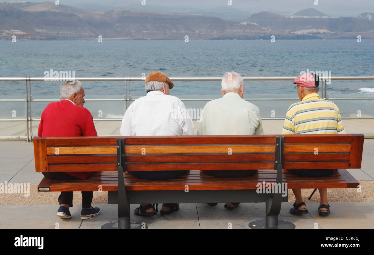 Four elderly men sitting on bench at coast In Spain Stock Photo