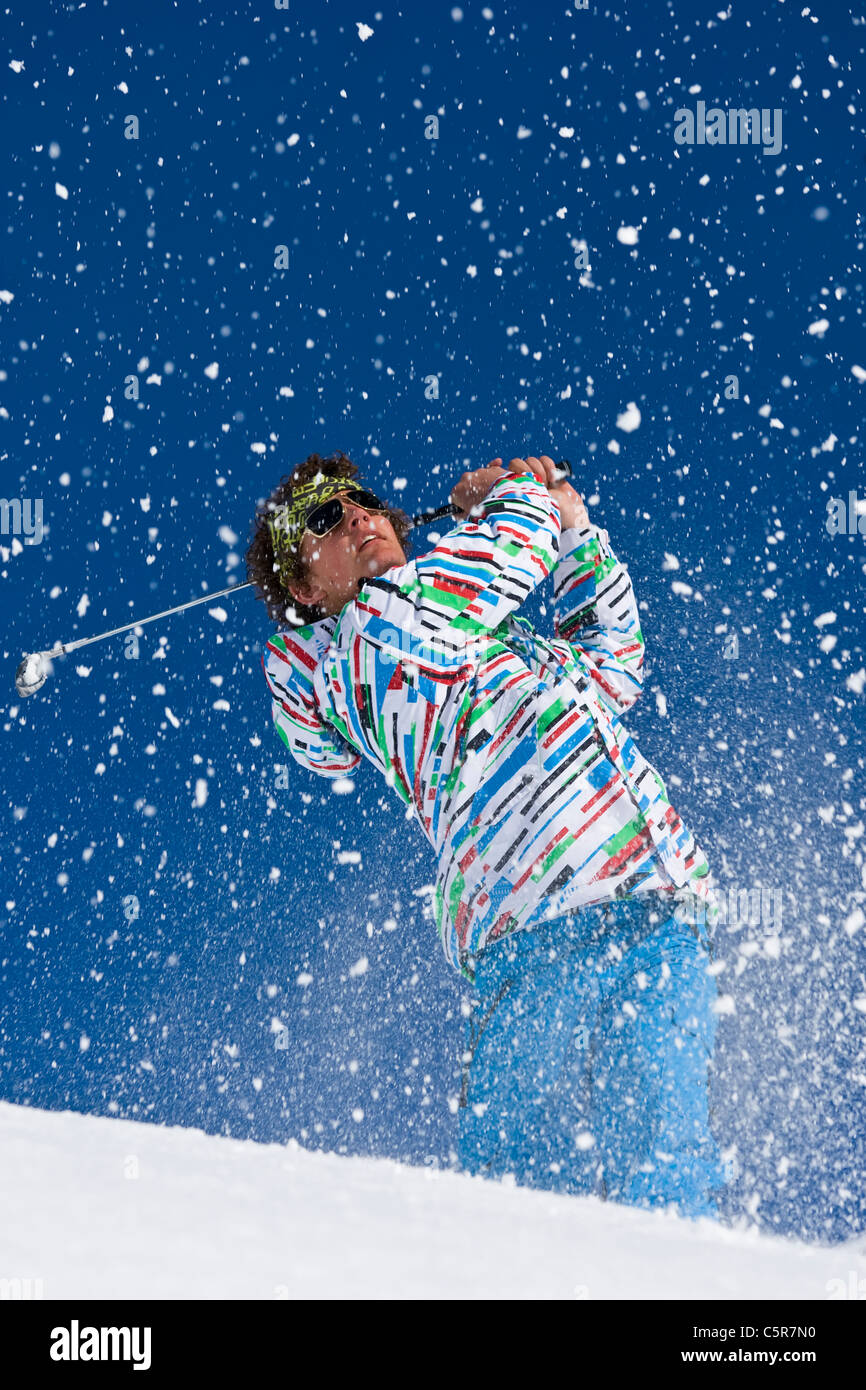 A golfer drives and follows ball on snowy alpine course. Stock Photo