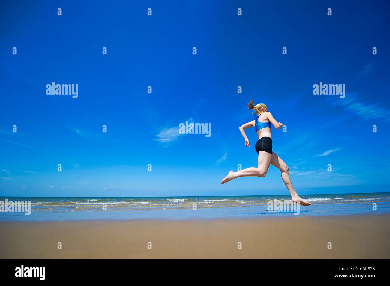 An athlete jogging barefoot along a sandy Ocean beach. Stock Photo
