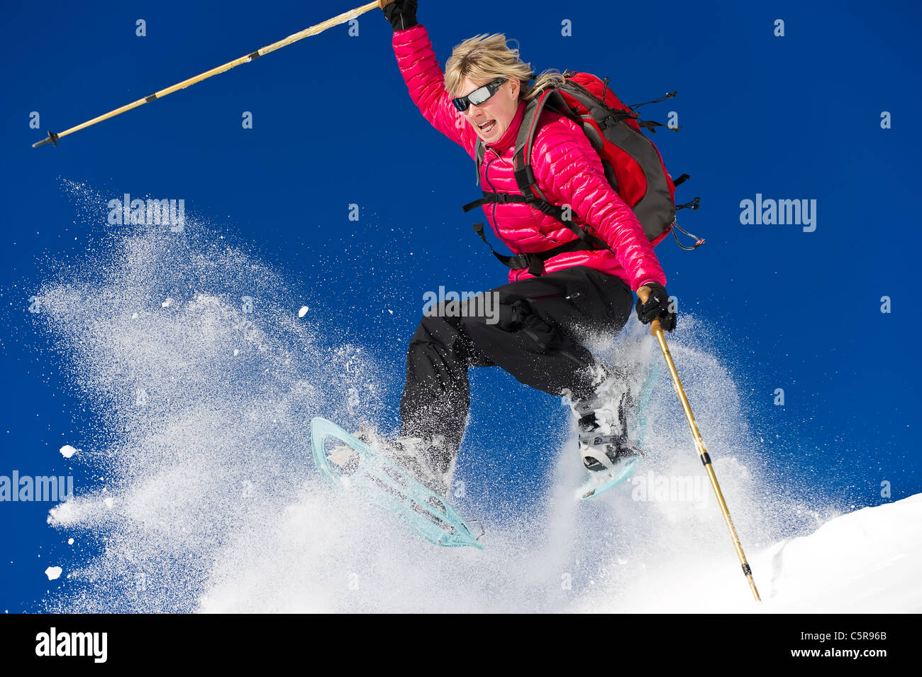 A woman snowshoeing leaps through fresh powder snow. Stock Photo