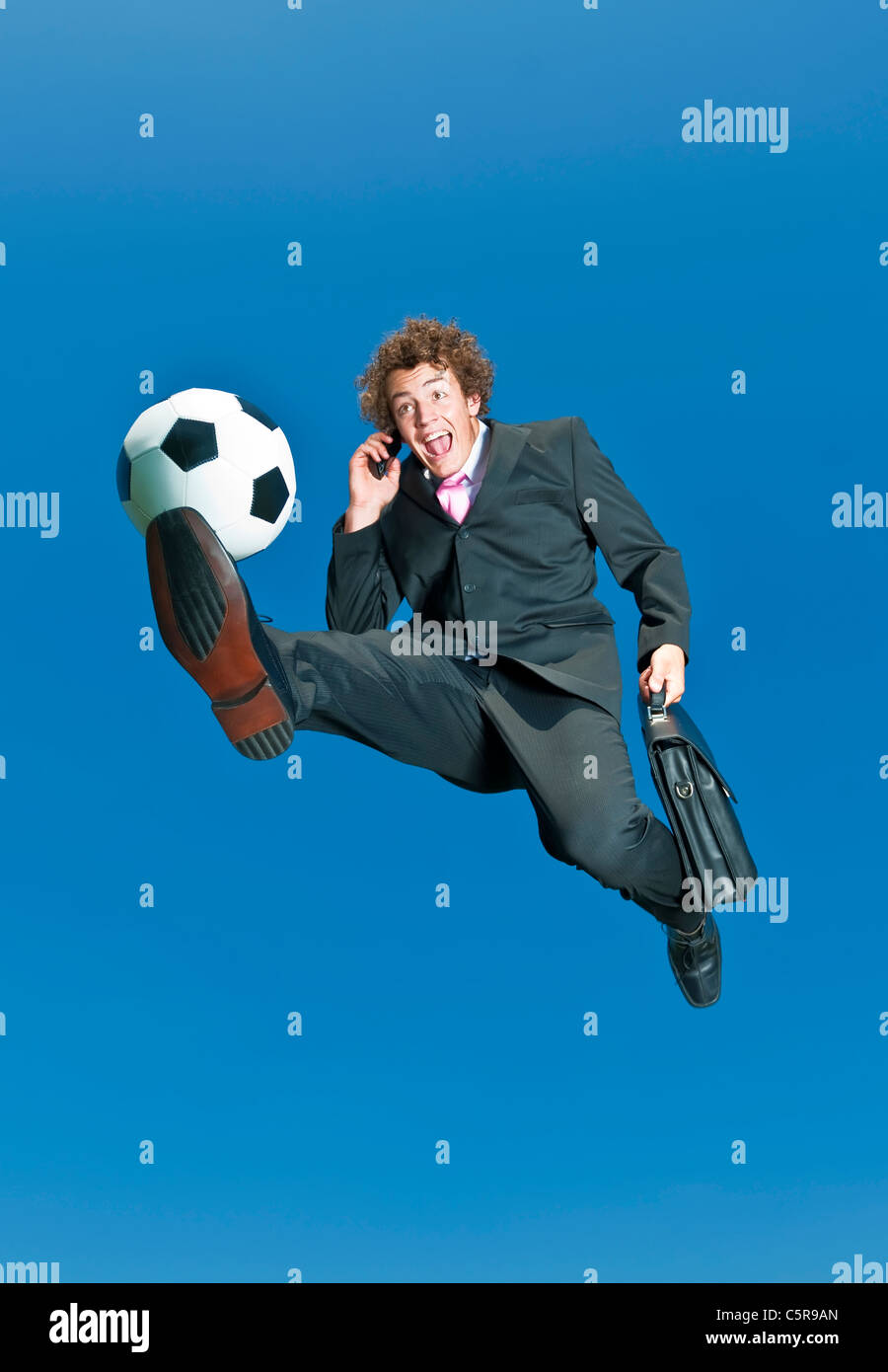 A businessman on a cell phone kicks ball. Stock Photo