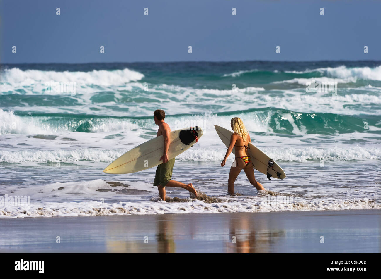 Two surfers heading out to the ocean waves. Stock Photo