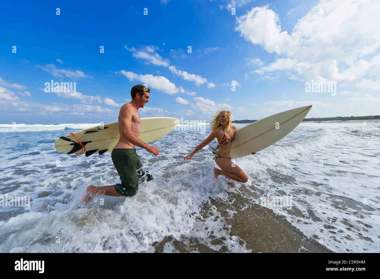 Two surfers run through the waves. Stock Photo