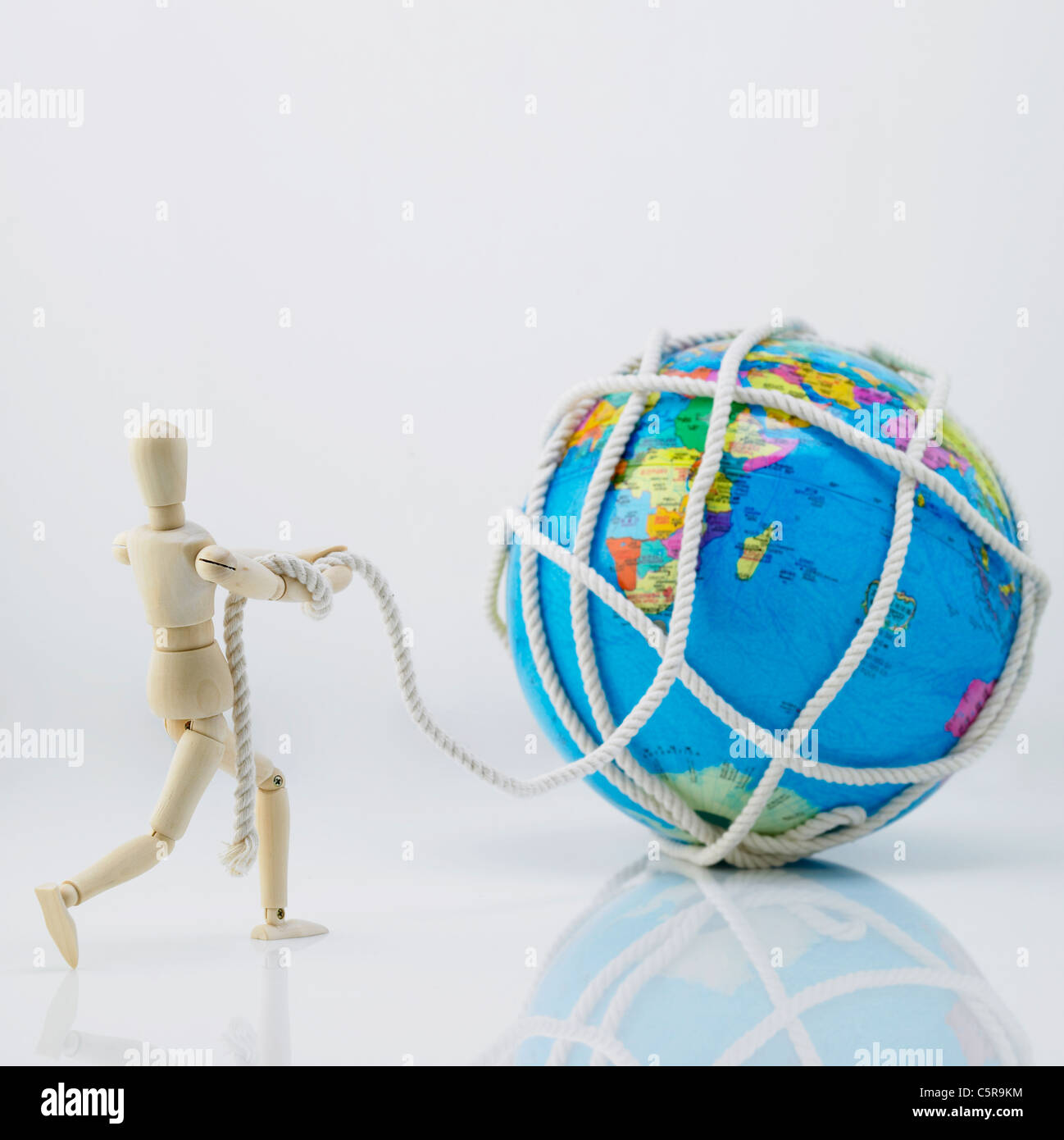 A wooden figurine pulling a globe rolled up by rope Stock Photo