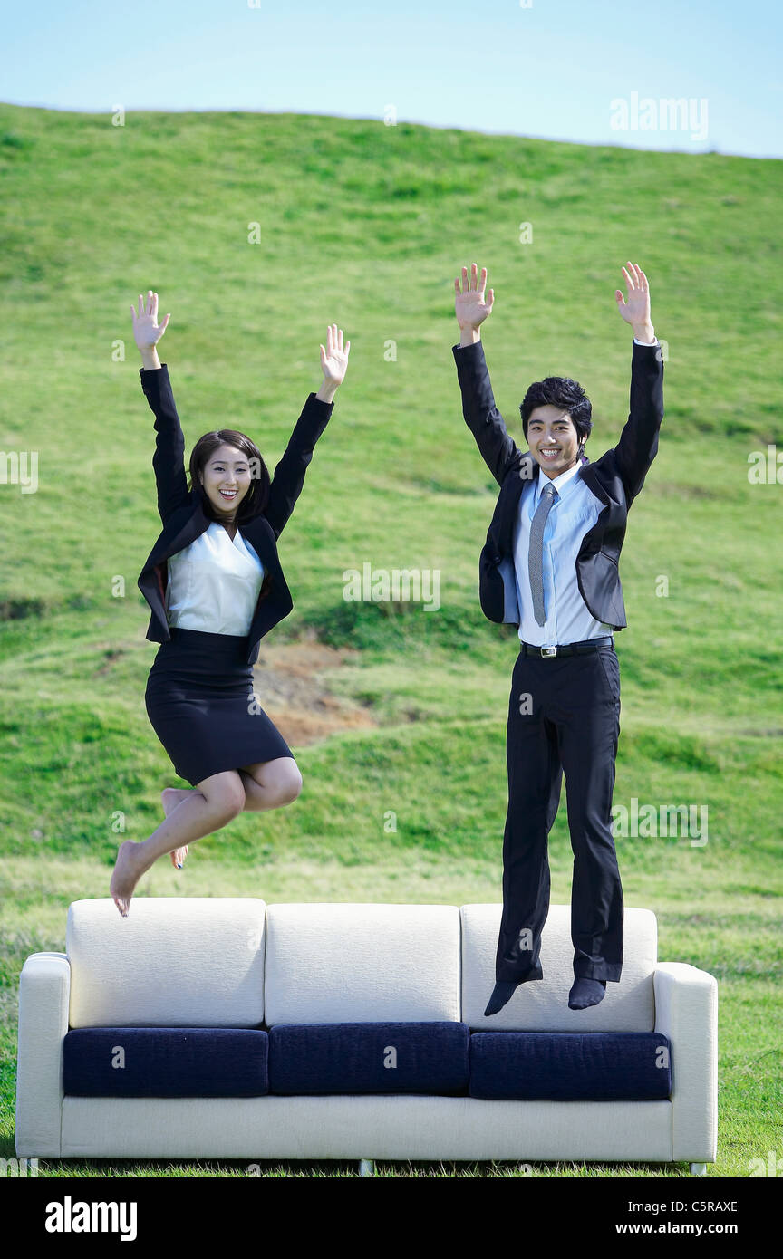 A man and a woman jumping on a sofa on grass Stock Photo