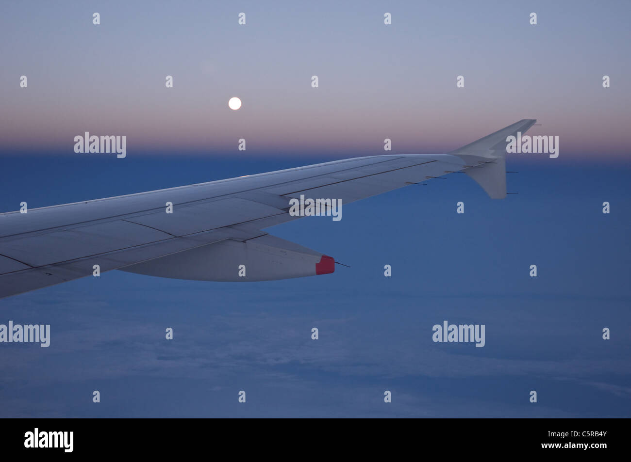 Airplane flying through the blue sky, clouds and moon. Stock Photo