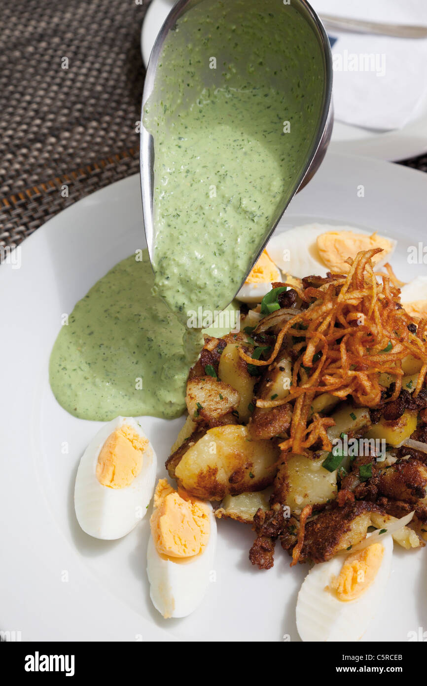 Close up of hard boiled eggs with roasted potatoes, onions and pouring Frankfurter Sauce Stock Photo