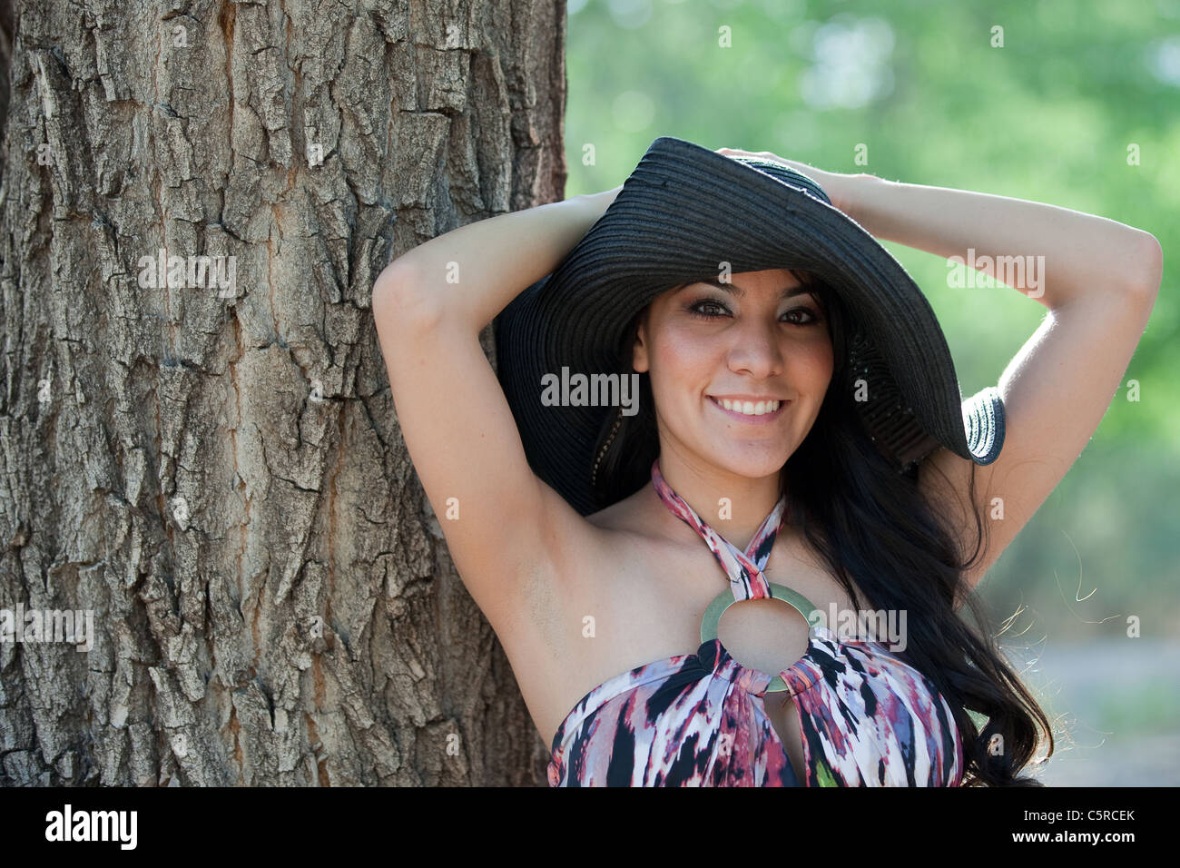 Happy Hispanic young woman leaning against a tree, outdoors Stock Photo ...