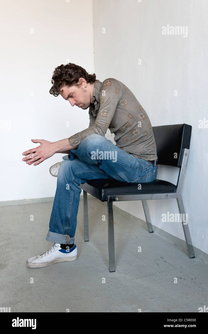 Mid adult man sitting on chair and looking down Stock Photo
