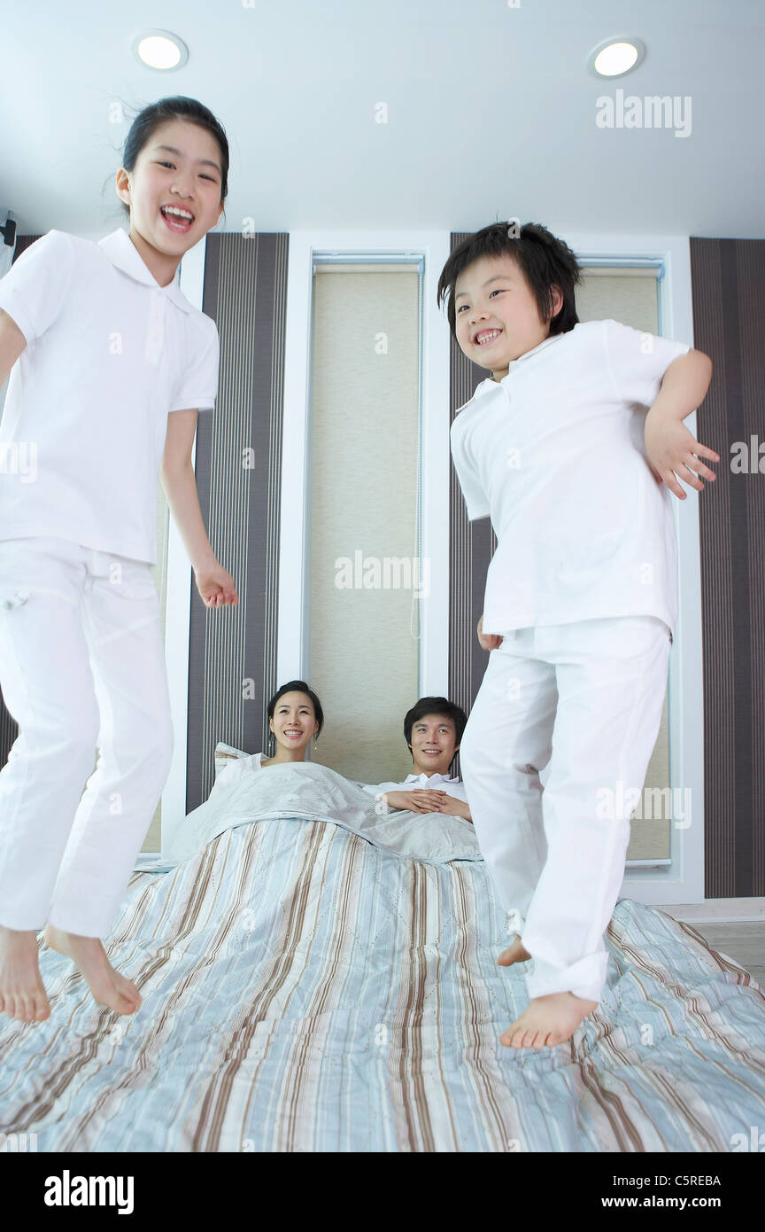 Two children jumping on the bed where their parents are lying down Stock Photo