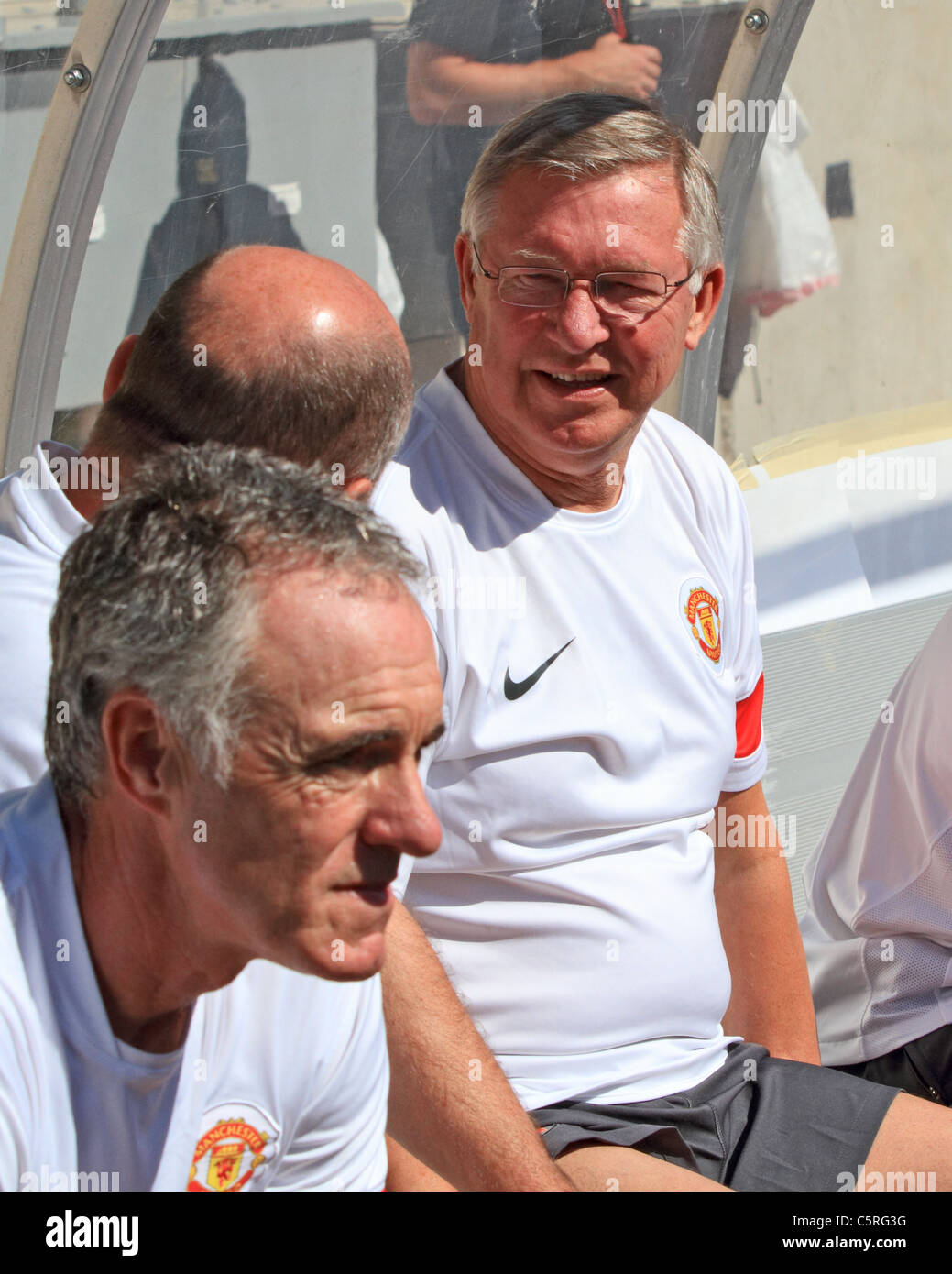 Manchester United manager, Sir Alex Ferguson (R), chats with his coaches on the bench, vs. the Chicago Fire, at Soldier Field. Stock Photo