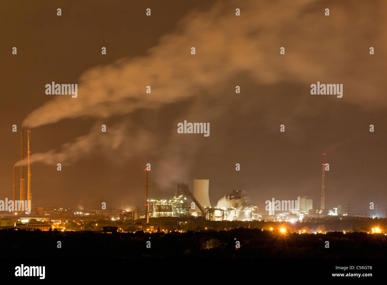 Germany, Nordrhein-Westfalen, Duisburg, View of smoke stacks of industrial plant at night Stock Photo