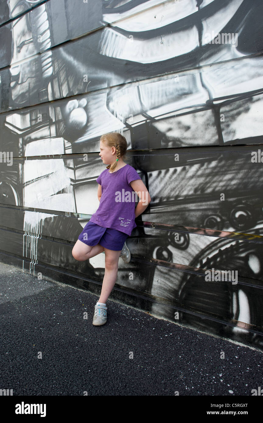 Young girl in purple top leaning against wall displaying monochrome graffiti in Chamonix Mont Blanc, France. Stock Photo