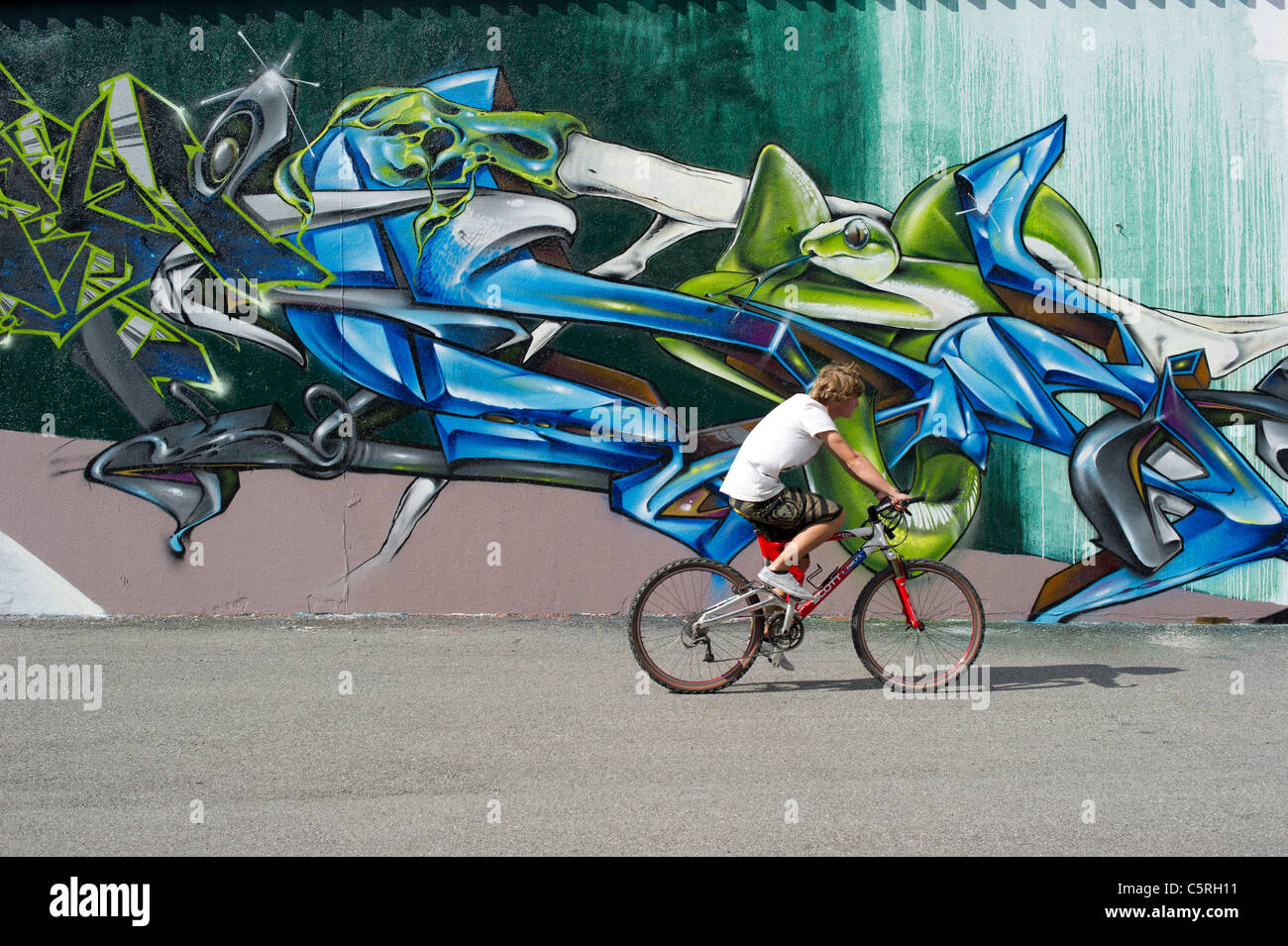 A youth on a mountain bike cycling past a wall of graffiti in Chamonix Mont Blanc, France. Stock Photo