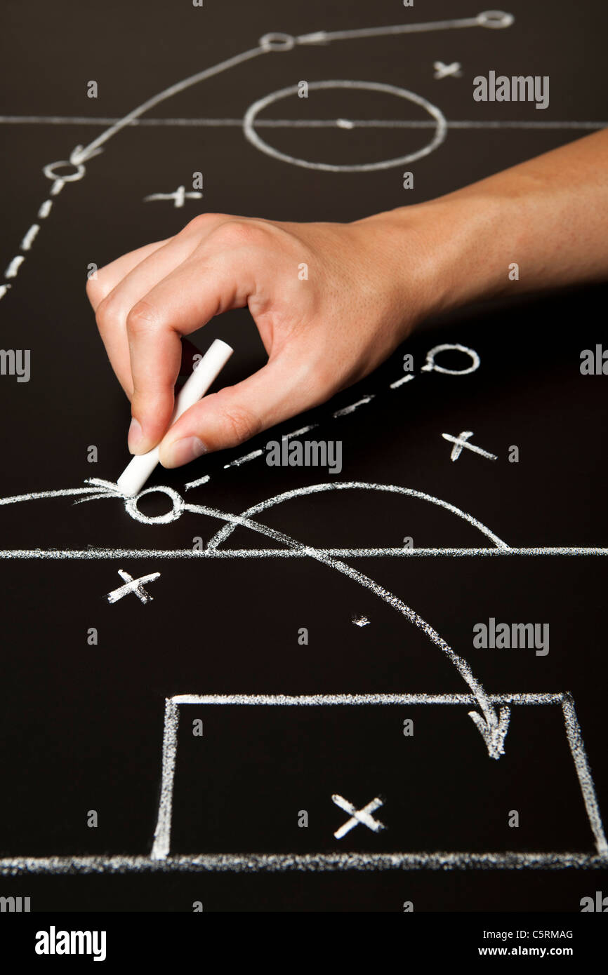 Hand drawing a soccer game strategy with white chalk on a blackboard. Stock Photo