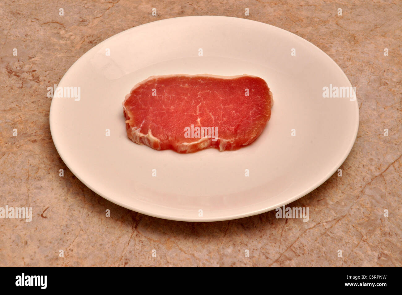 A slice of pork tenderloin lays on a white saucer Stock Photo