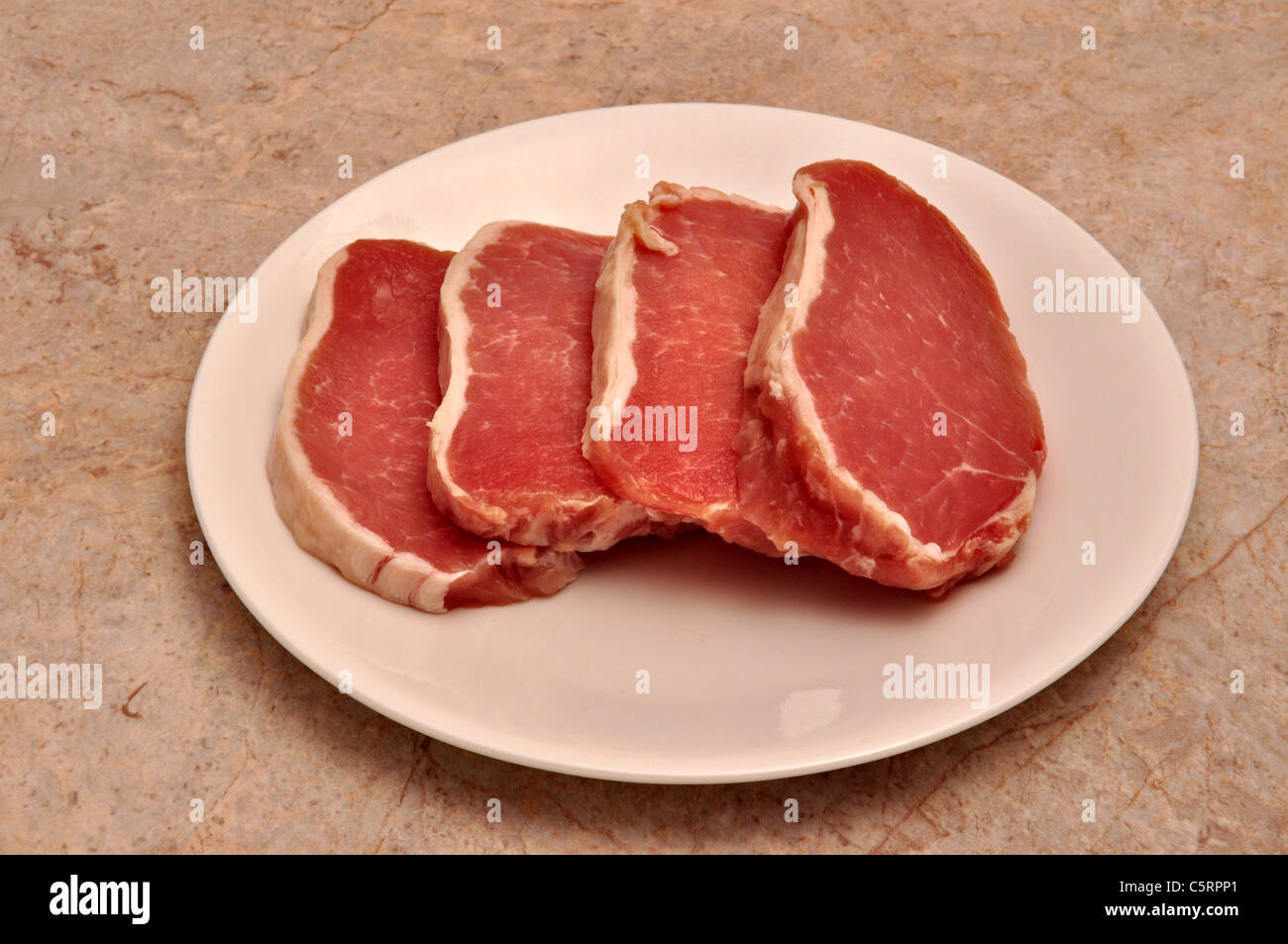 Four slices of pork tenderloin lay on a white saucer Stock Photo