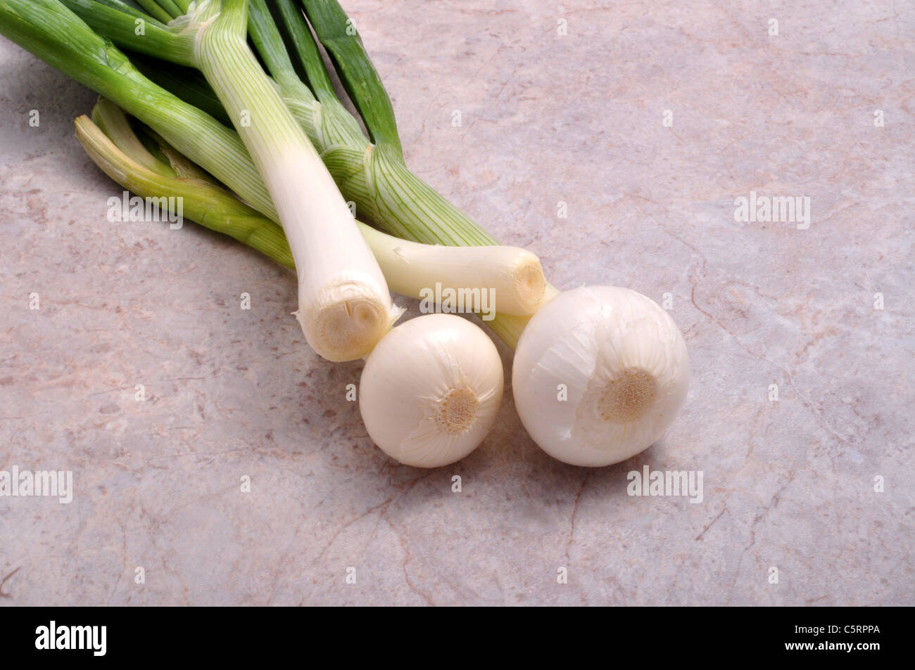 A bunch of four green onions lay on top of a table Stock Photo