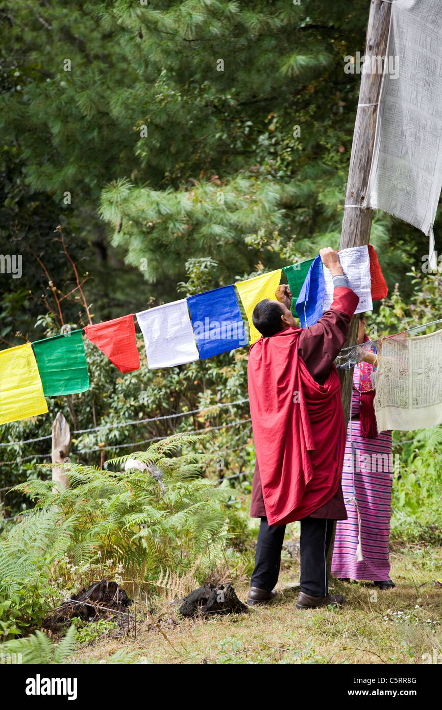 Monk tying new prayer flags outside monastery en route Tiger’s nest monastery near Paro, Bhutan Stock Photo