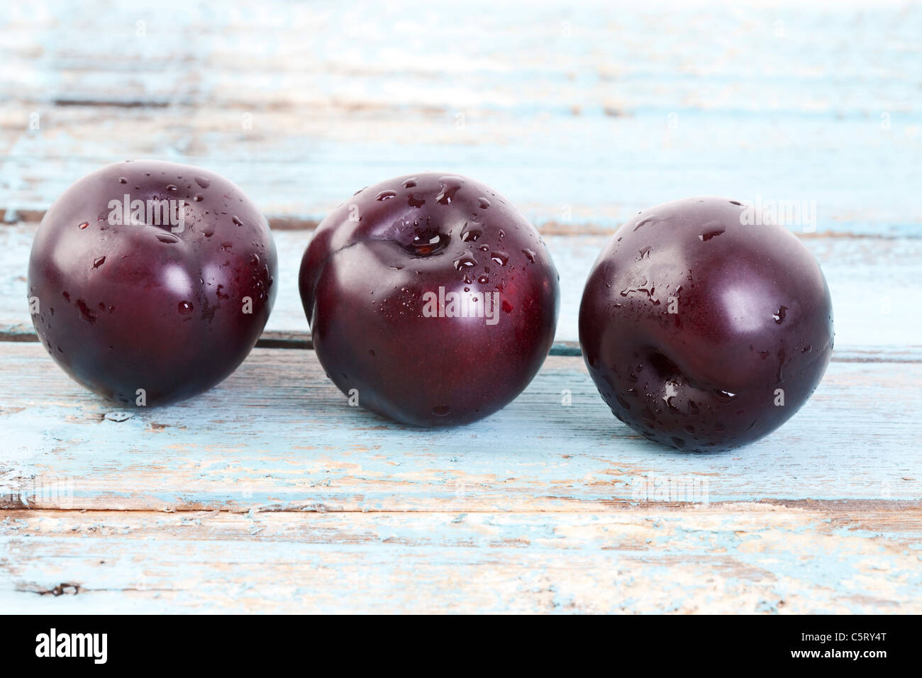 Three plums on wooden table, close up Stock Photo