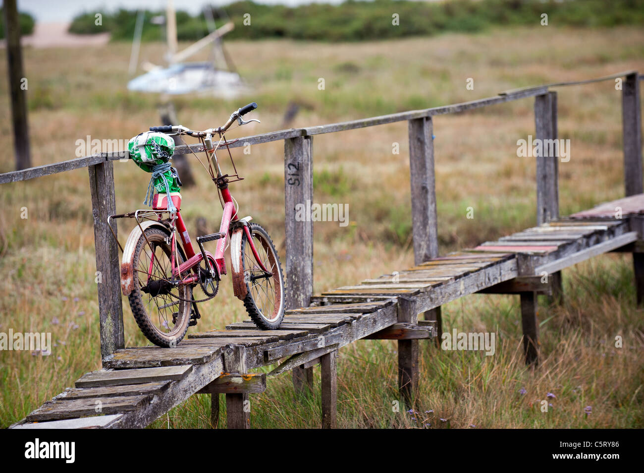 An old bicycle leaning against a rickety wooden walkway on Mersea Island in Essex. Stock Photo