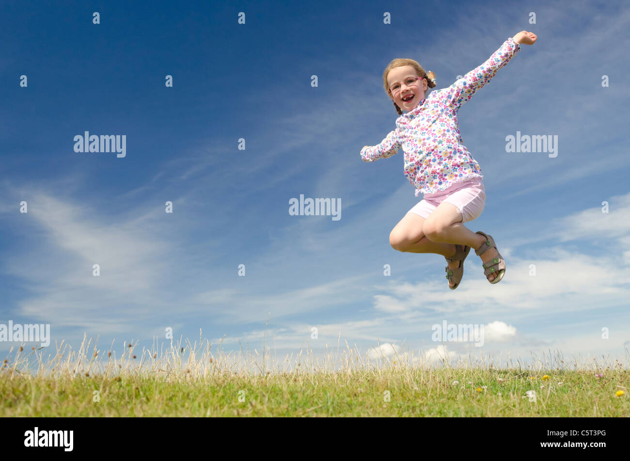 Happy little girl jumping in front of blue sky Stock Photo - Alamy