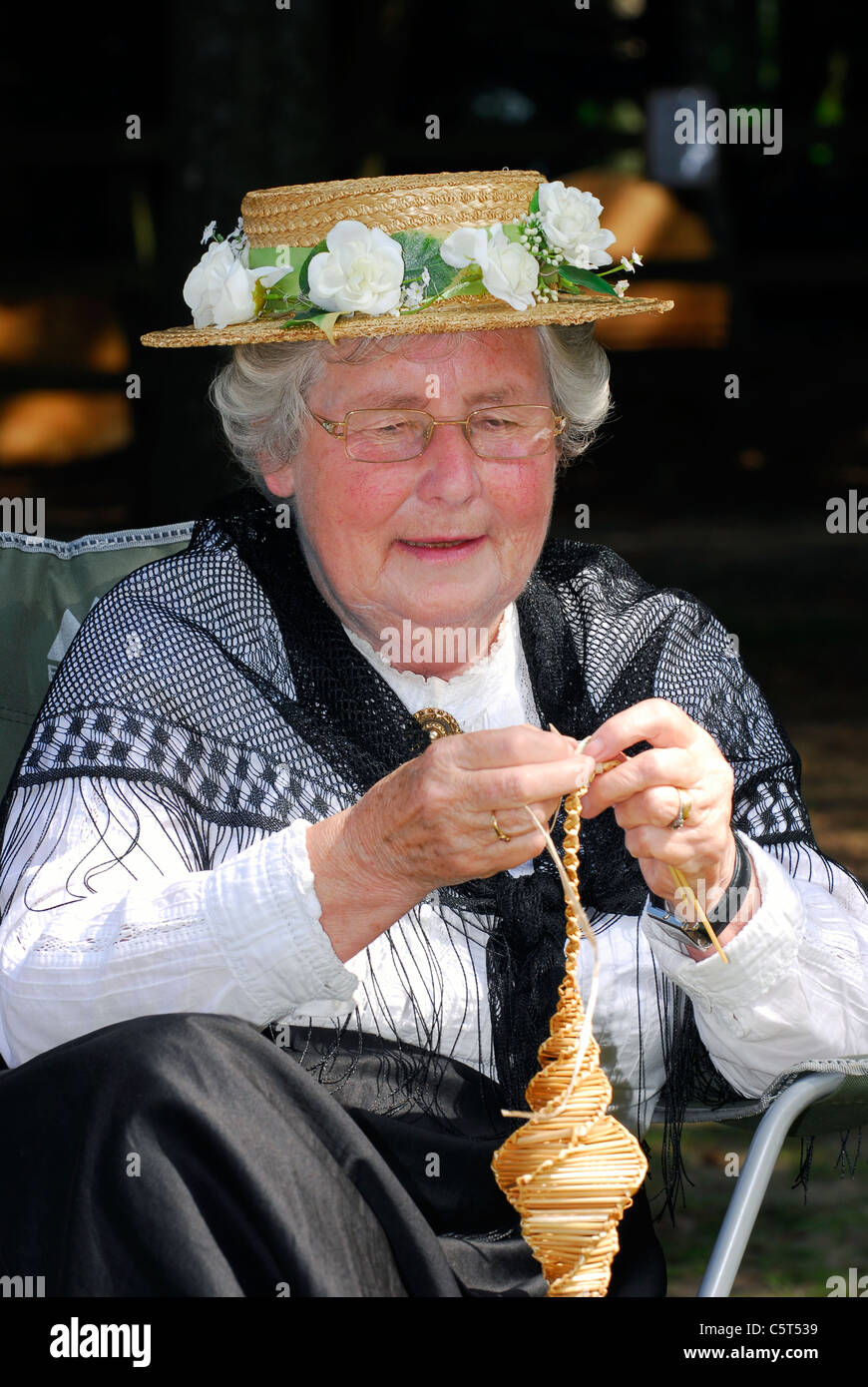 Elderly lady in Victorian costume at Rustic Sunday making a corn dolly, Rural Life Centre, Tilford, near Farnham, Surrey, UK. Stock Photo