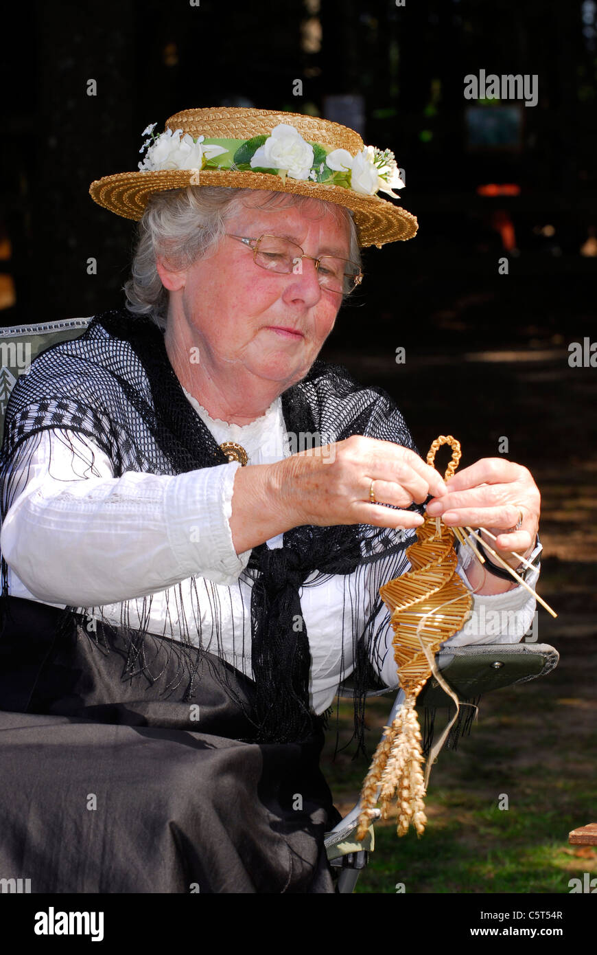 Elderly woman in Victorian costume at Rustic Sunday making a corn dolly, Rural Life Centre, Tilford, near Farnham, Surrey, UK. Stock Photo