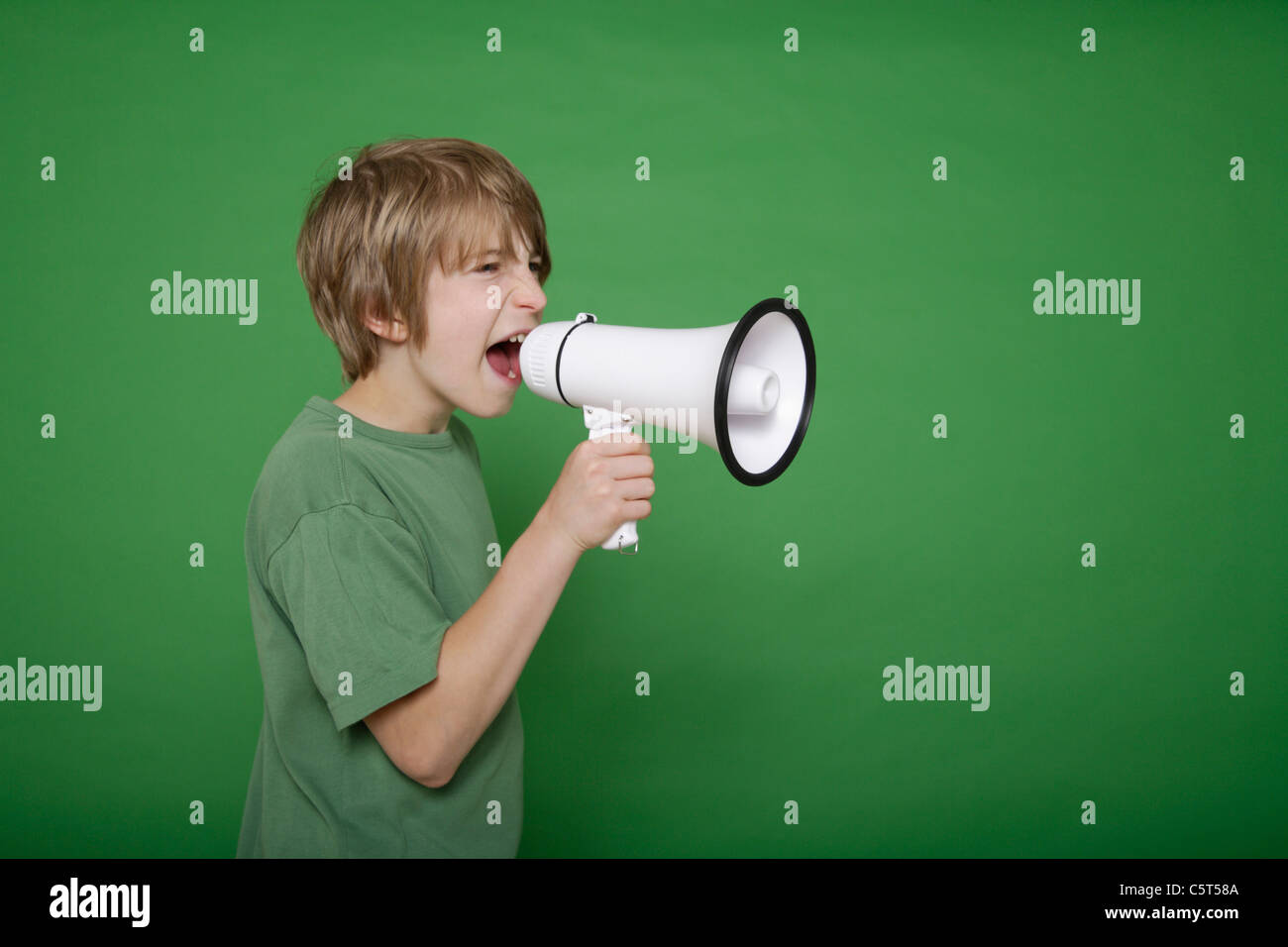 Boy screaming in megaphone against green background Stock Photo