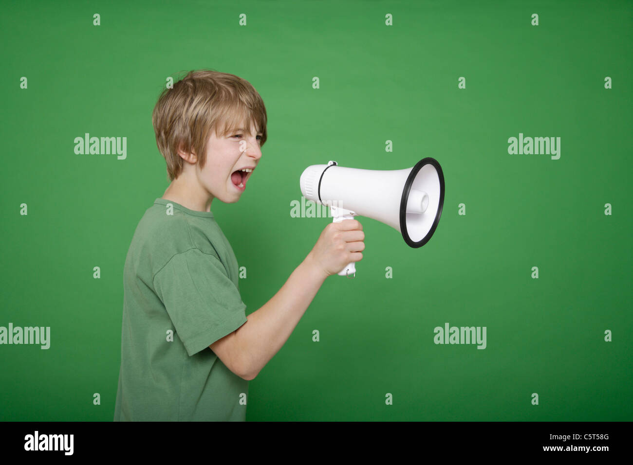 Boy screaming in megaphone against green background Stock Photo