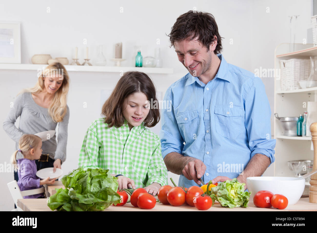 Germany, Bavaria, Munich, Son preparing salad with father, mother and daughter in background Stock Photo