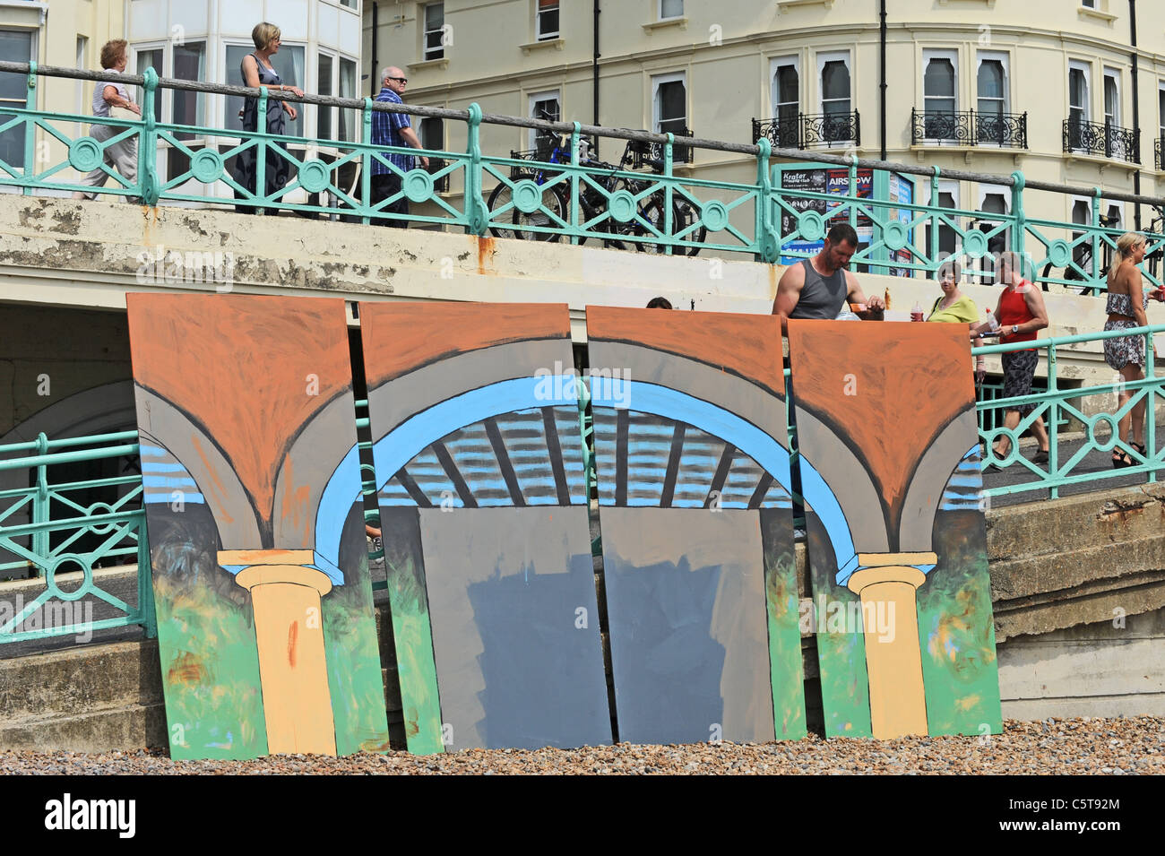 A man paints a large piece of artwork showing the seafront arches along Brighton beach today Stock Photo