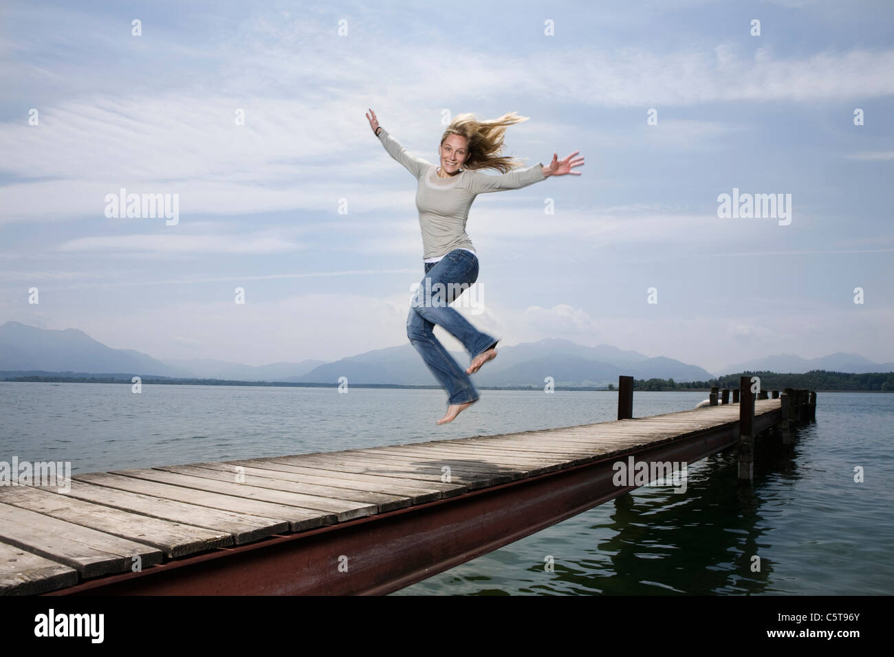 Germany, Chiemsee, Woman jumping on jetty Stock Photo